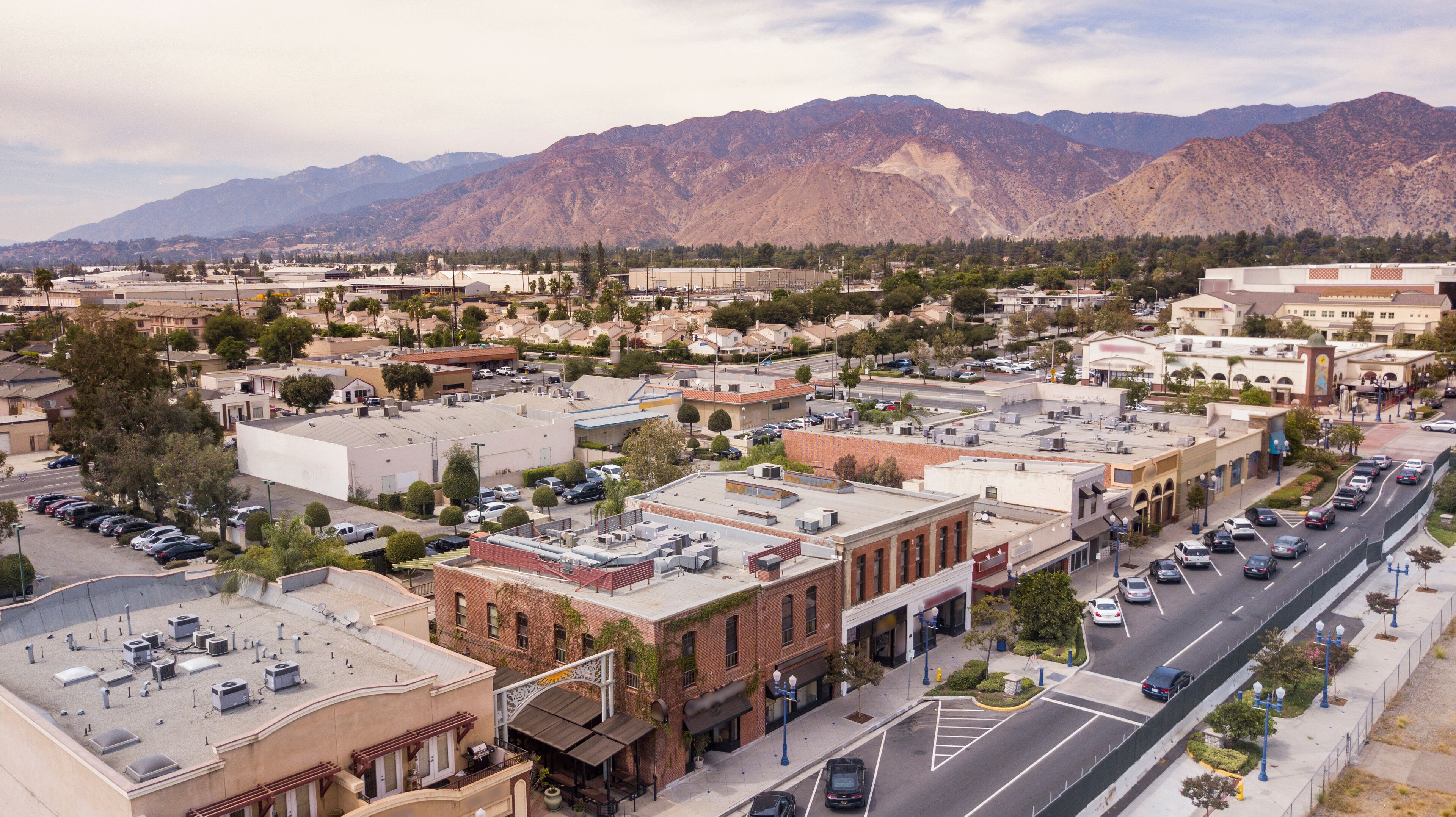 A town with a mountain range in the background, a main street with parked cars, and several buildings with flat roofs.