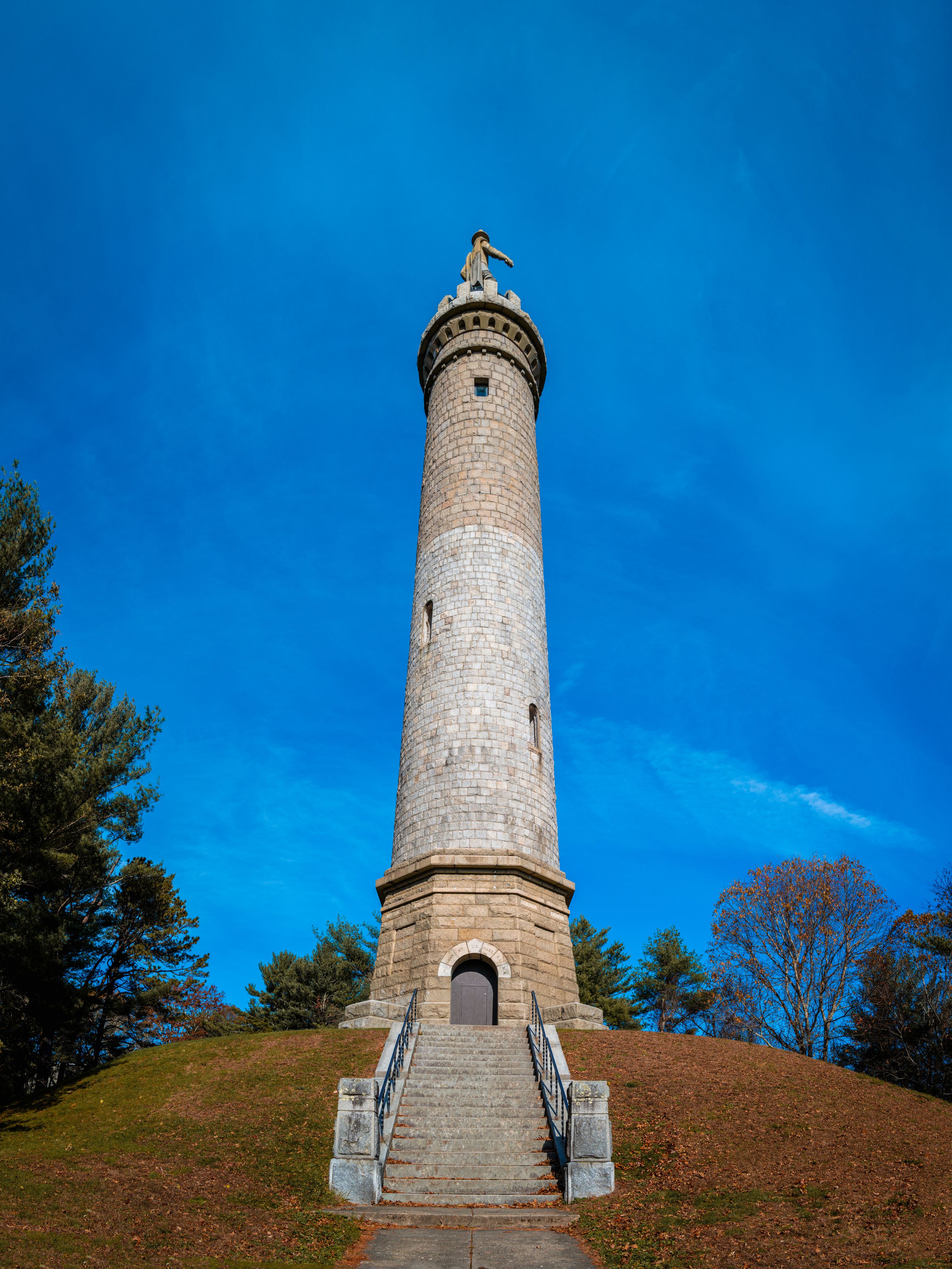 Tall Myles Standish Monument over the hill on the vibrant blue sky background.