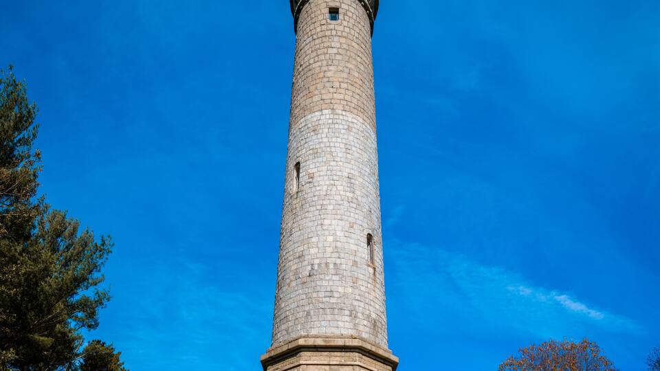 Tall Myles Standish Monument over the hill on the vibrant blue sky background.