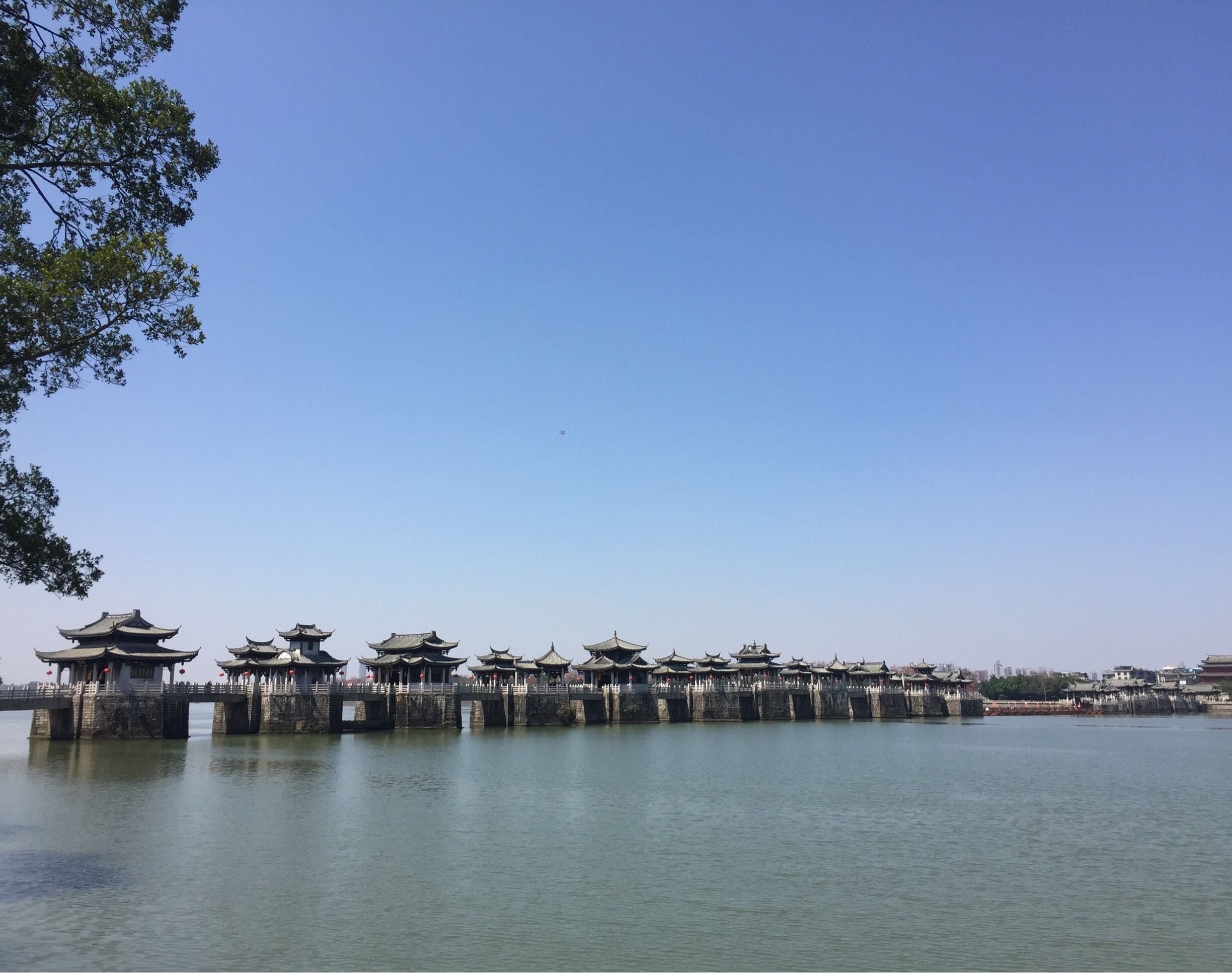 Un pabellón chino tradicional sobre un río tranquilo, bajo un cielo azul despejado.