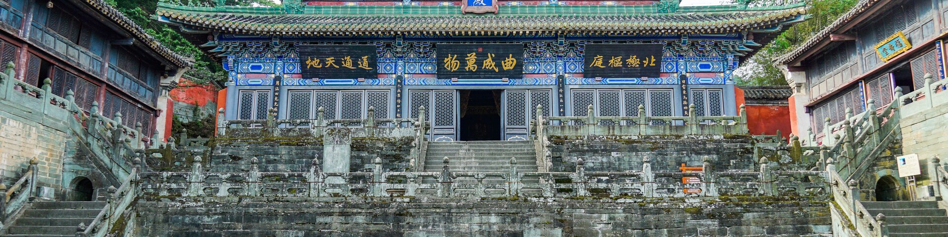 Un edificio chino tradicional con decoraciones ornamentales en azul y oro, una amplia escalera que conduce a la entrada y un farol de piedra en primer plano.