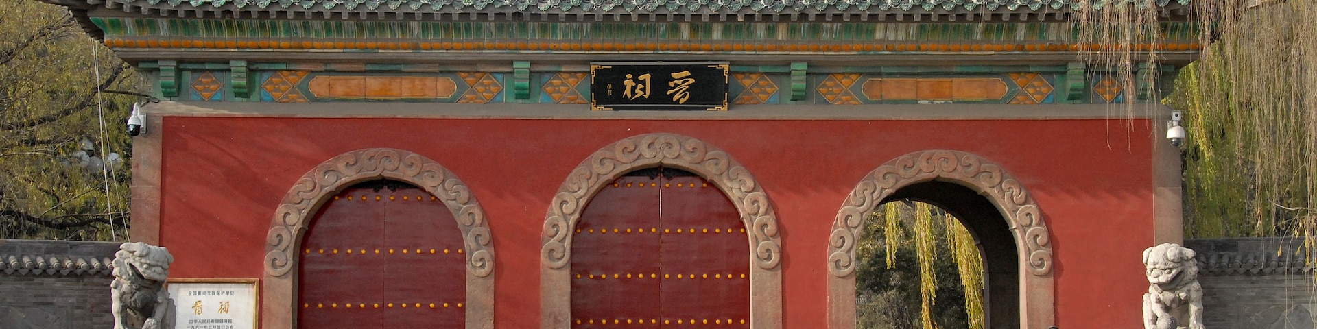 Un edificio tradicional chino con tejas ornamentales, grandes puertas rojas y estatuas de leones de piedra.