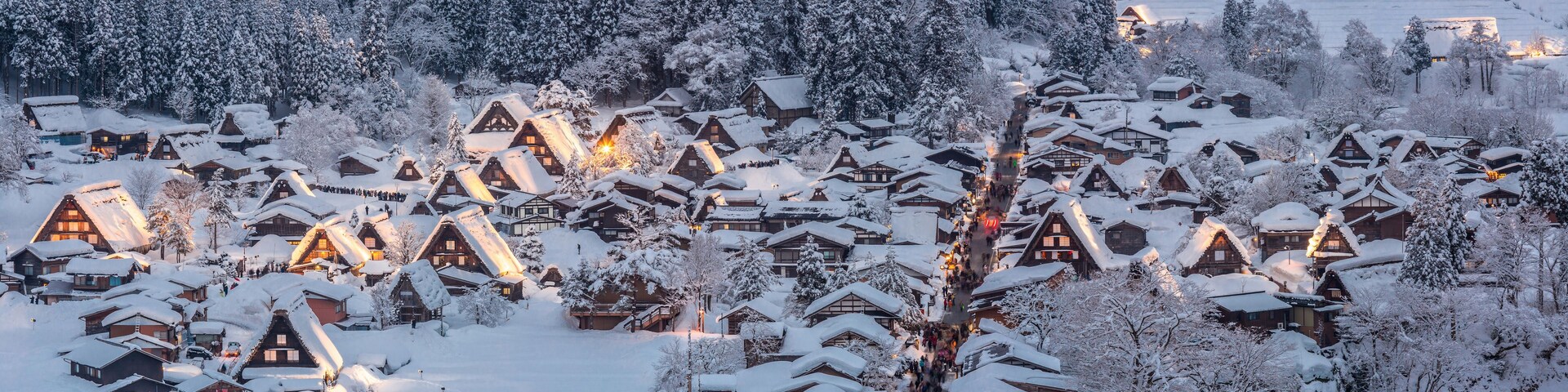 Un pueblo cubierto de nieve con casas de madera y un bosque al fondo.