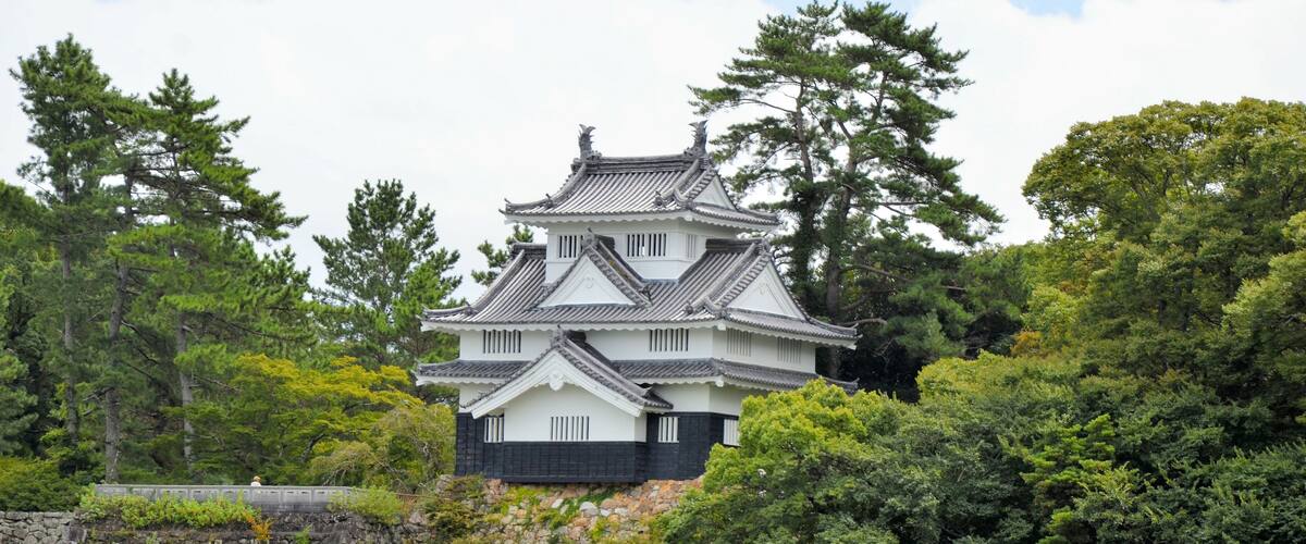 A traditional Japanese castle with multiple tiers, surrounded by lush greenery and trees.