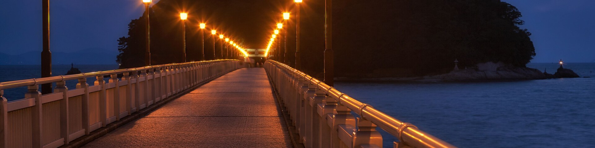 Uma passarela noturna com postes de luz que levam a uma colina.