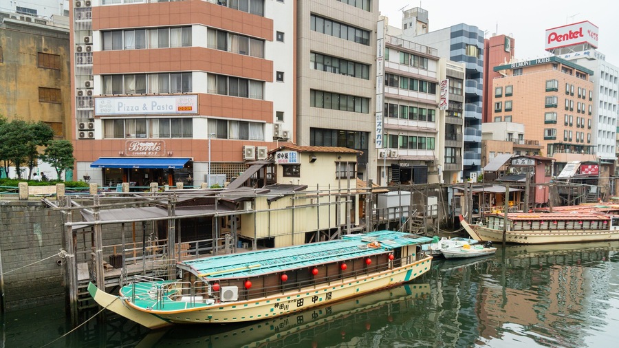 A river with boats docked, surrounded by buildings including a hotel and a restaurant.