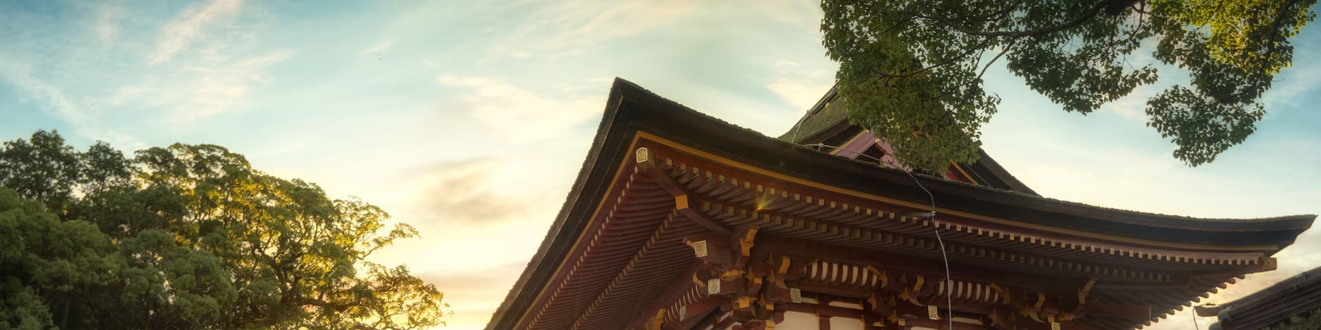 A traditional Japanese temple with a multi-tiered pagoda, surrounded by lush greenery and a clear sky.