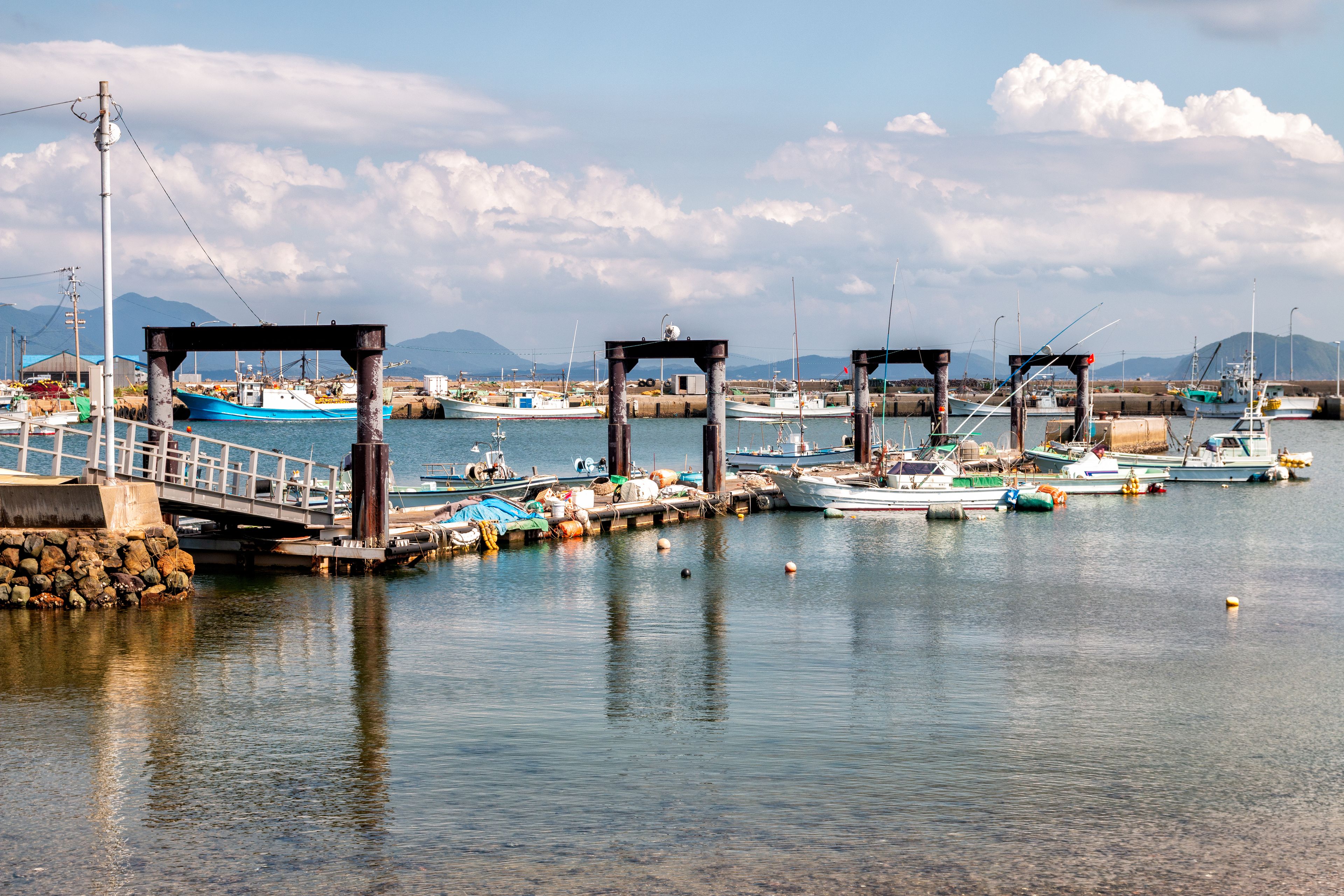 A harbor with boats docked, a bridge, and mountains in the background.