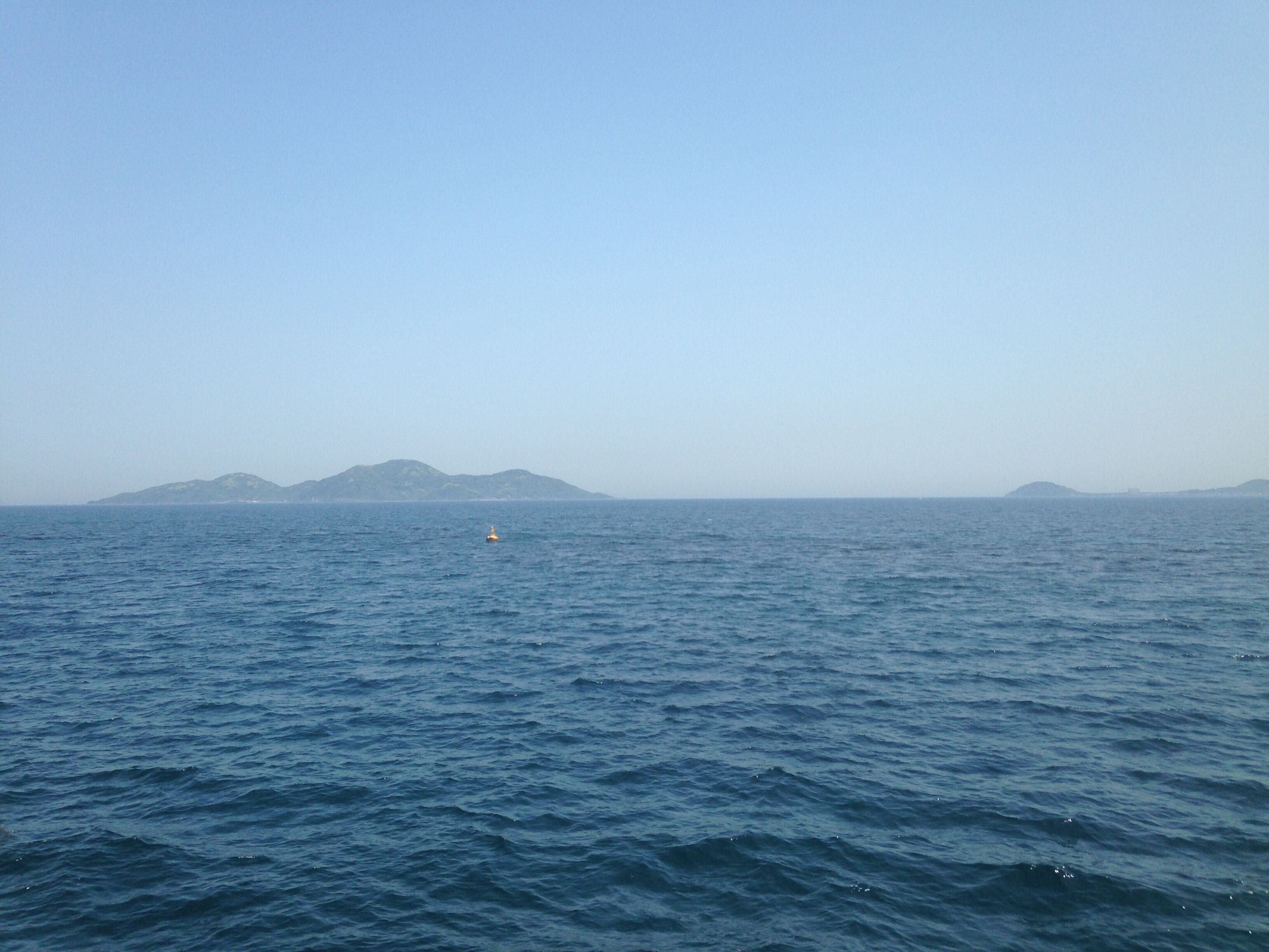 A calm sea with a buoy and distant islands.