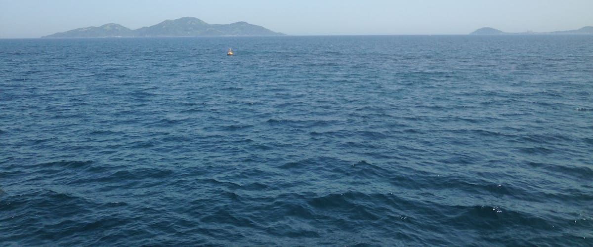 A calm sea with a buoy and distant islands.