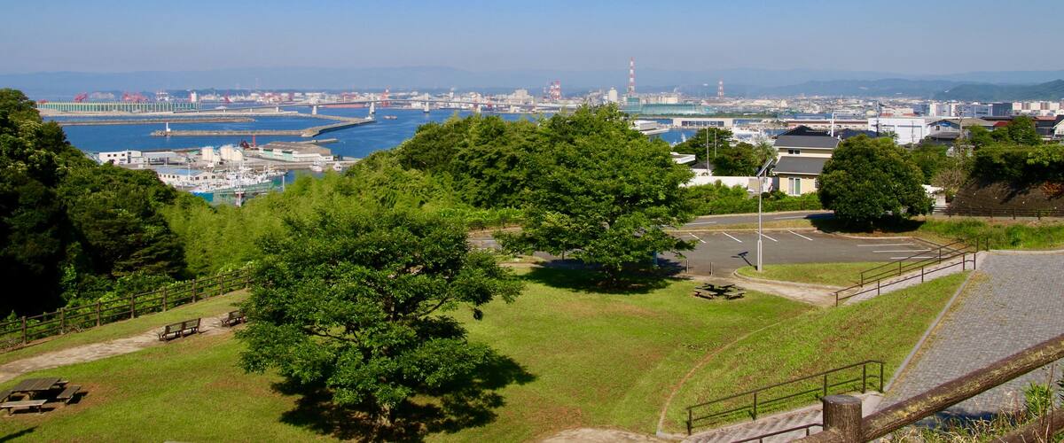 A coastal cityscape with a marina, green hills, and a clear blue sky.