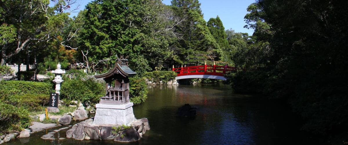 A serene Japanese garden with a red bridge, a stone lantern, and lush greenery.