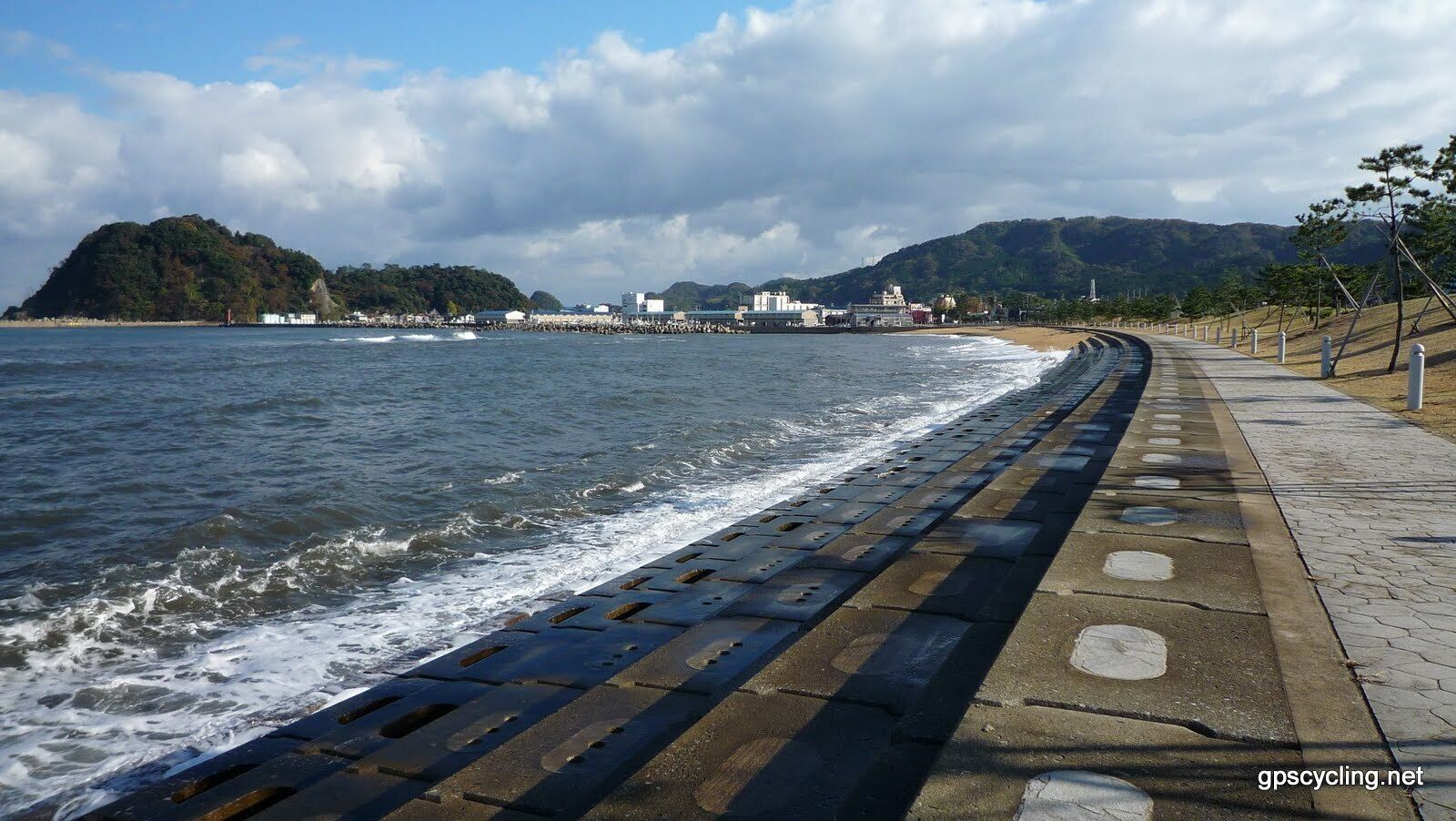 A coastal walkway with a sea wall, a beach, and a town in the background.