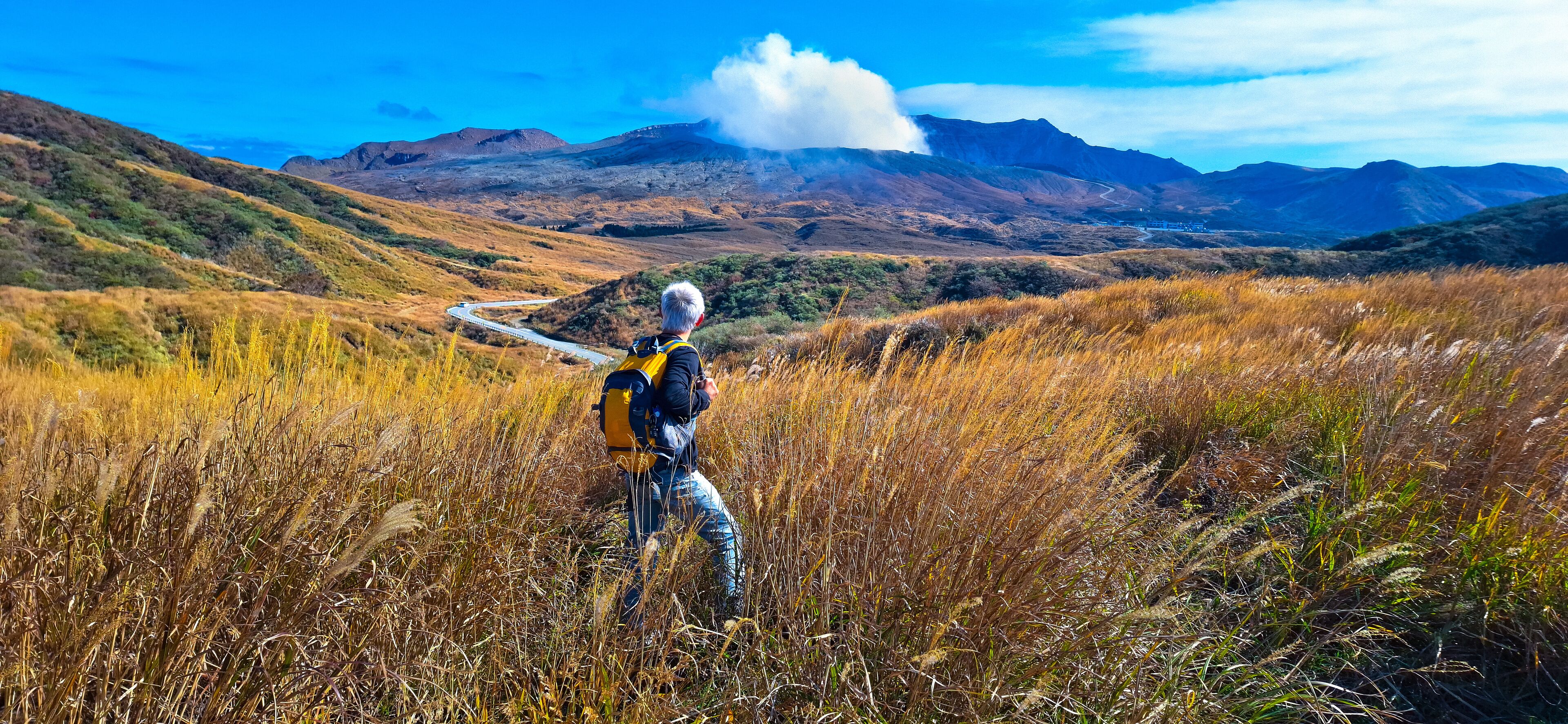 A hiker in a grassy field with a mountain range in the background.