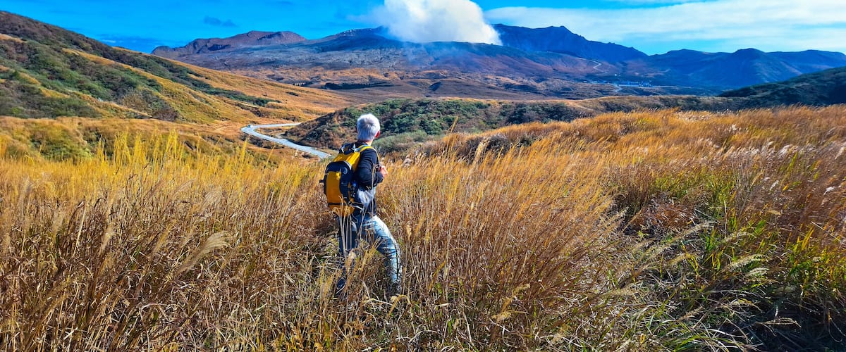 A hiker in a grassy field with a mountain range in the background.