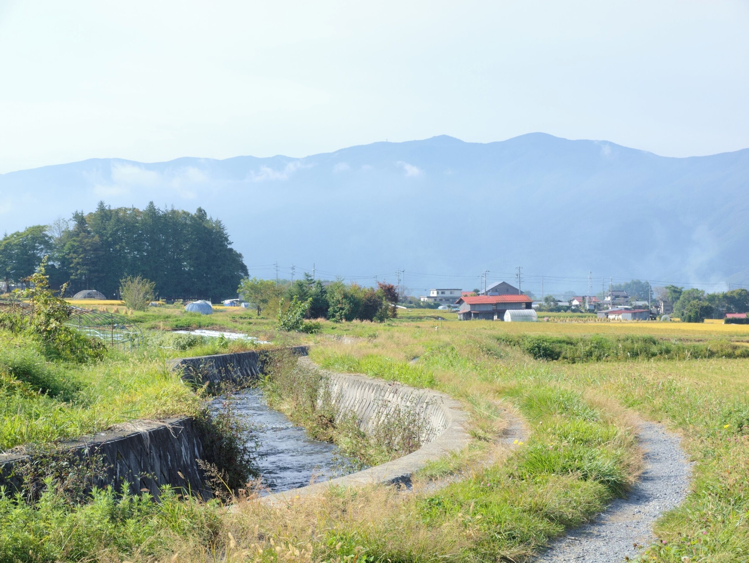 A rural landscape with a stream, fields, and houses.