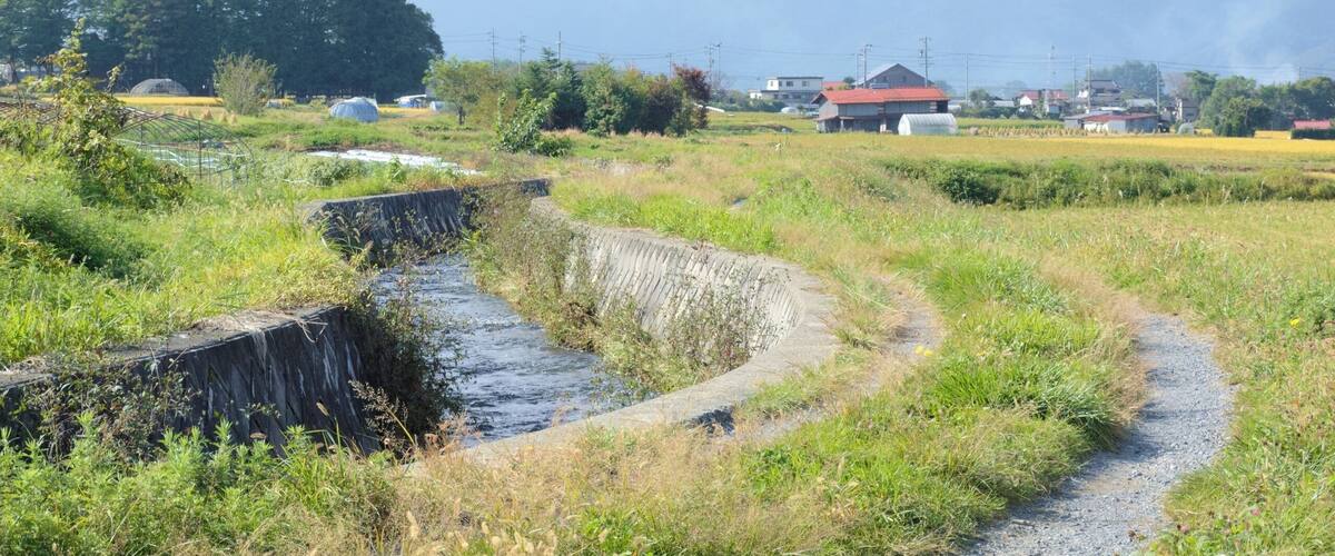 A rural landscape with a stream, fields, and houses.