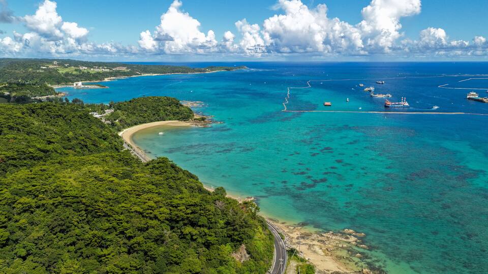A coastal landscape with a winding road, a beach, and a clear blue sea.