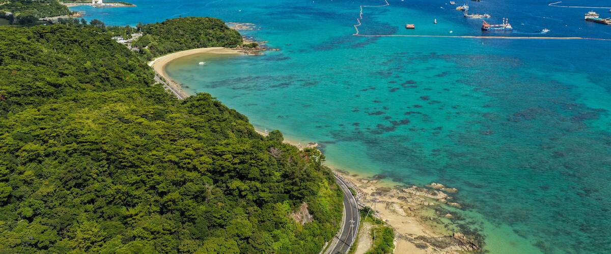 A coastal landscape with a winding road, a beach, and a clear blue sea.