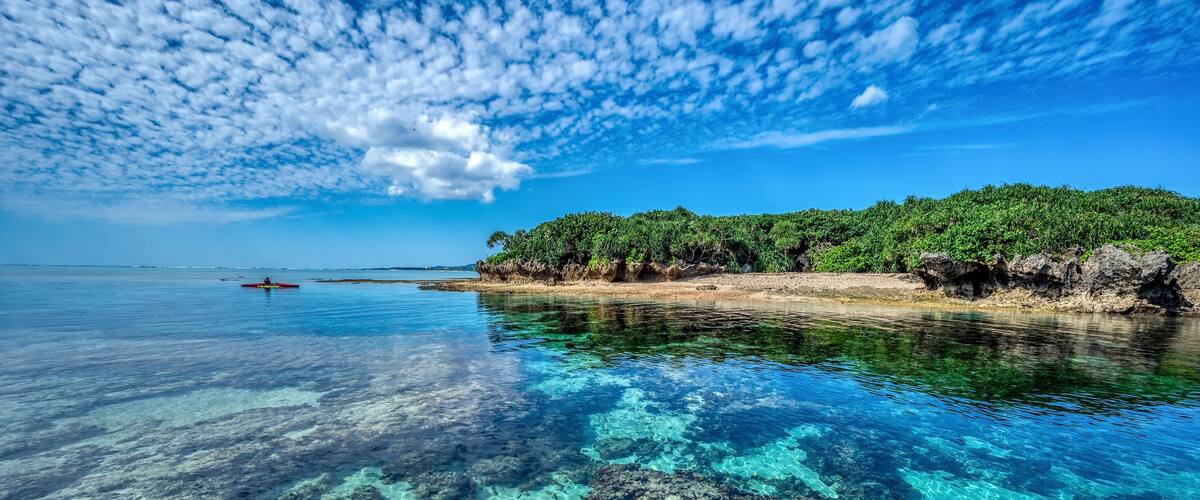 Crystal clear waters of Bise Beach, Motobu District, Okinawa main island. White sand beach with coral outcrops and small islands offshore.