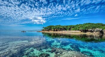 Mare blu intenso con una costa rocciosa, una piccola barca e un'isola lontana ricoperta da vegetazione.