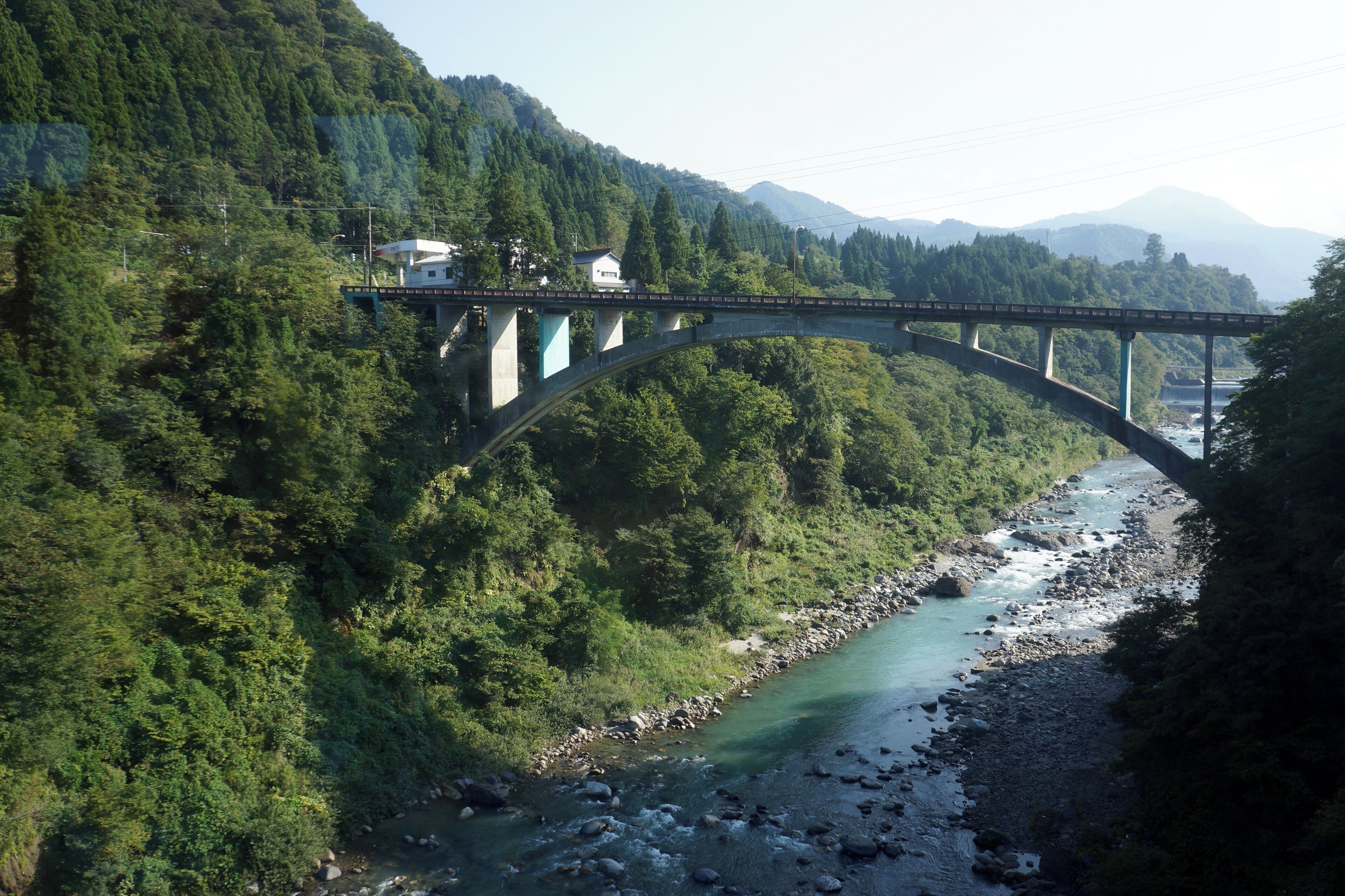 A bridge over a river surrounded by dense forest and mountains.