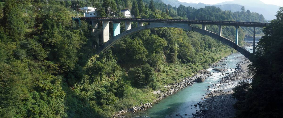 A bridge over a river surrounded by dense forest and mountains.