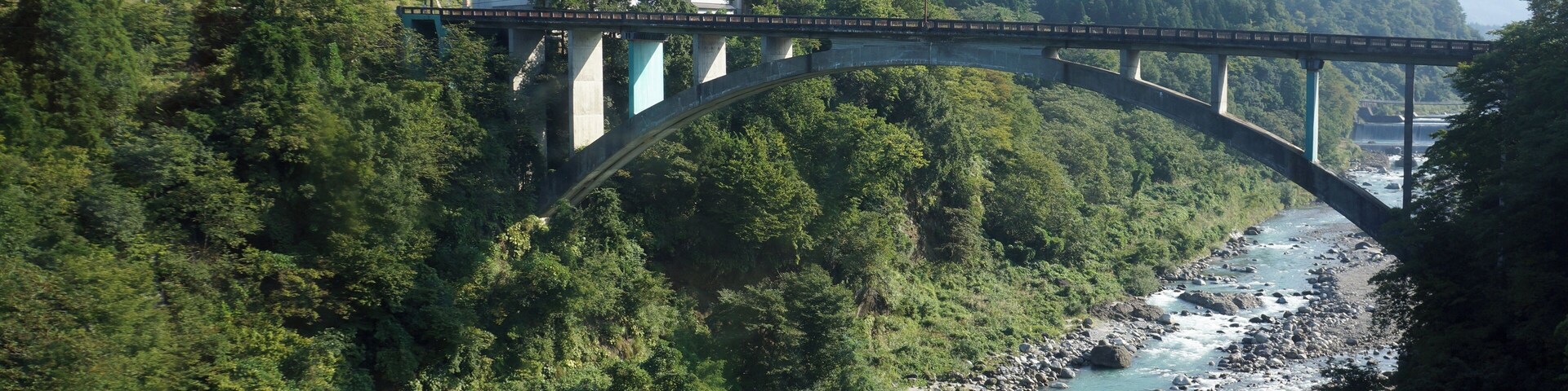 A bridge over a river surrounded by dense forest and mountains.