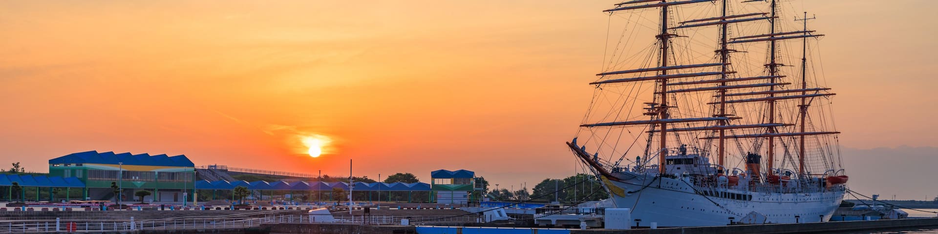A large sailing ship docked at a harbor during sunset.