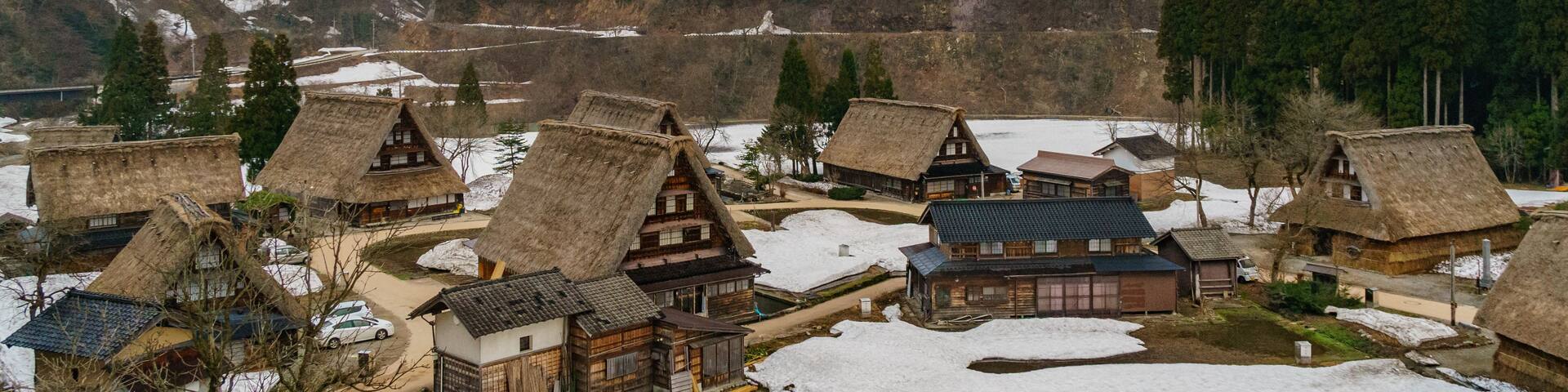 A village with traditional thatched-roof houses nestled in a snowy valley with mountains in the background.