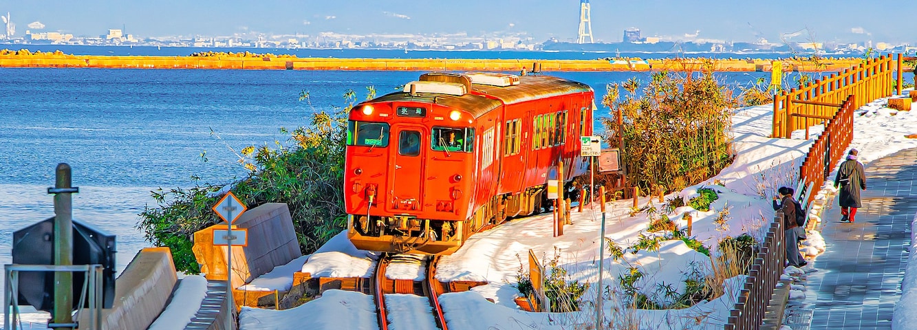 Um trem vermelho sobre trilhos, ao lado de um caminho nevado, com pessoas na calçada.