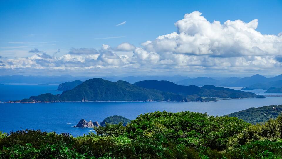 A coastal landscape with mountains, a clear blue sky, and a calm sea.