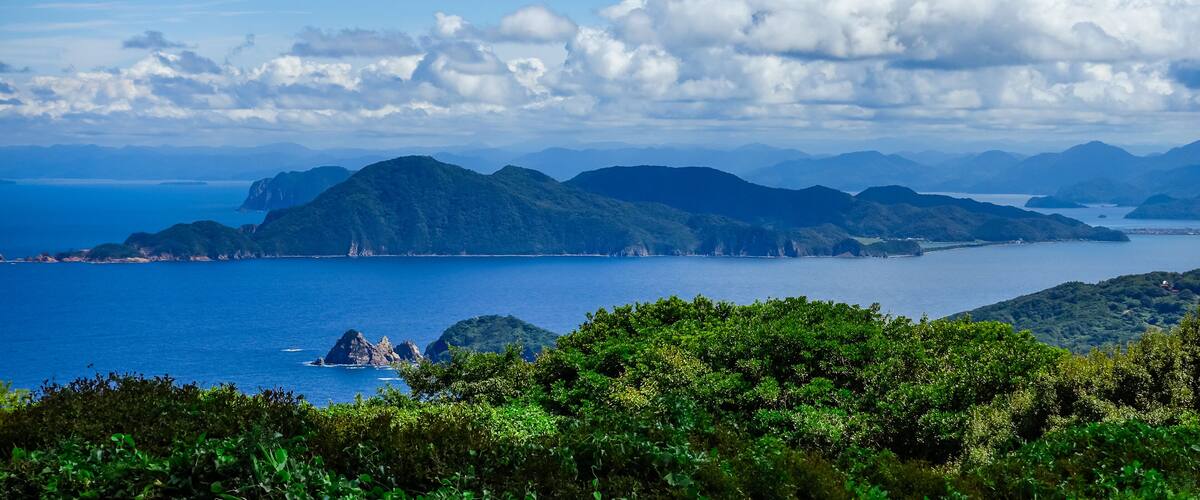 A coastal landscape with mountains, a clear blue sky, and a calm sea.