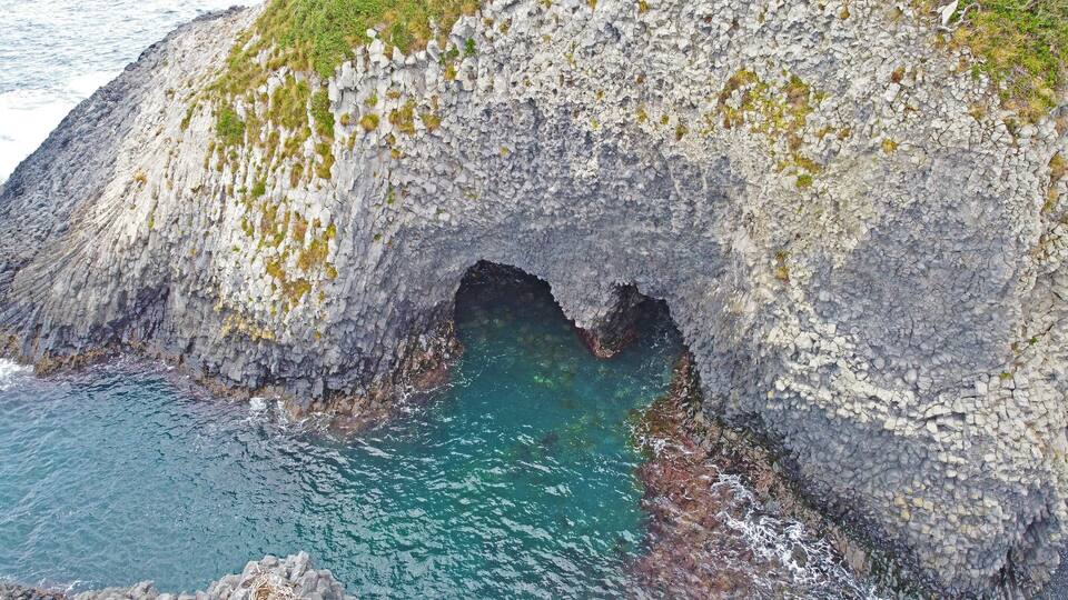 A rugged coastal cliff with a natural arch formation.