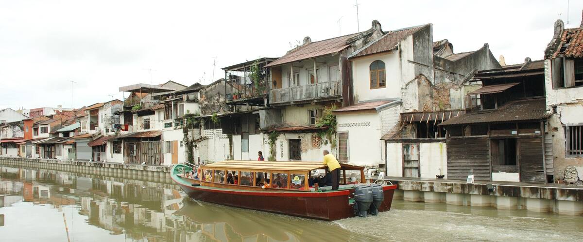 A narrow canal with a boat carrying passengers, surrounded by old buildings with traditional architecture.