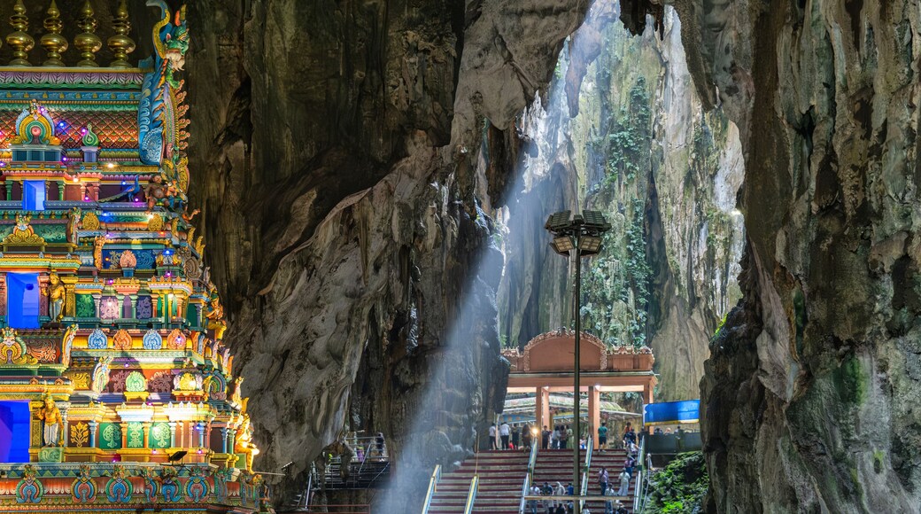Batu Caves interior with main Hindu Temple, Selangor, Malaysia. Tourists visiting Batu cave complex illuminated by natural light streaming through the cave's opening, Kuala Lumpur