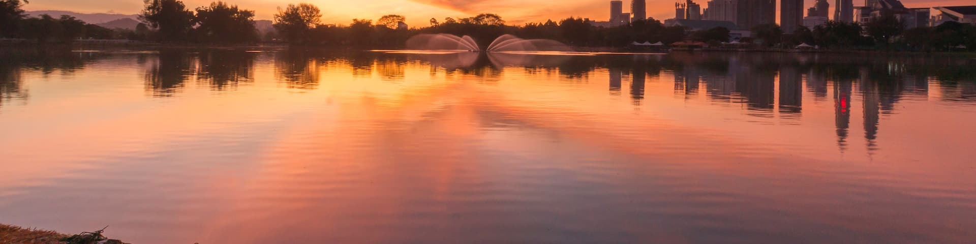 A sunset over a calm lake with a city skyline in the background.