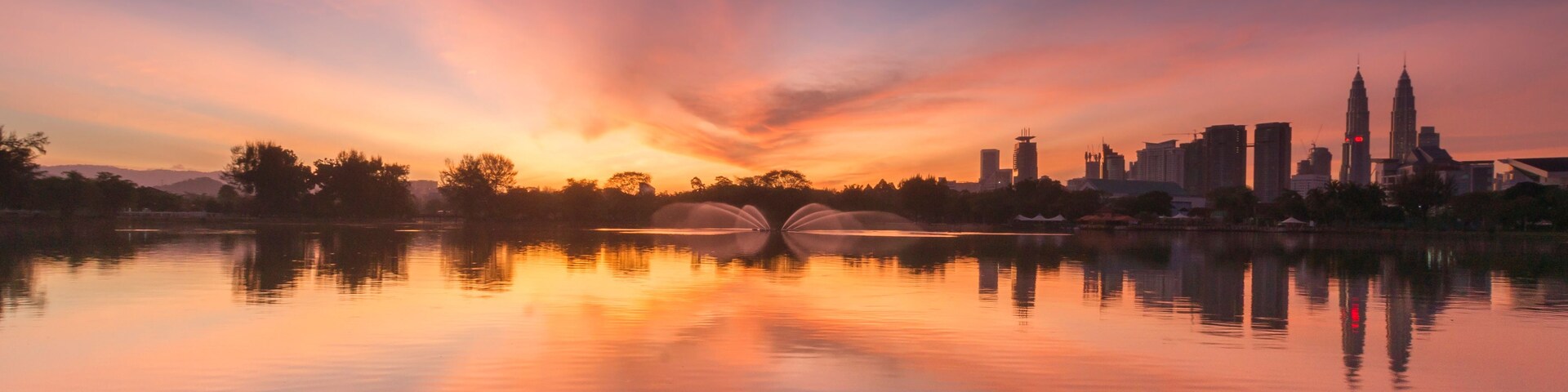 Un atardecer sobre un lago tranquilo con el horizonte de una ciudad al fondo.