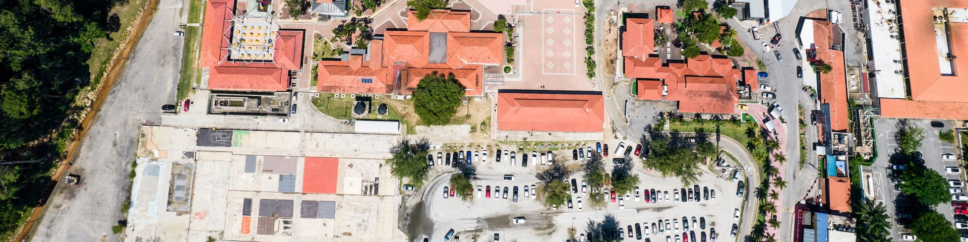 An aerial view of a coastal town with a beach, buildings, and parked cars.