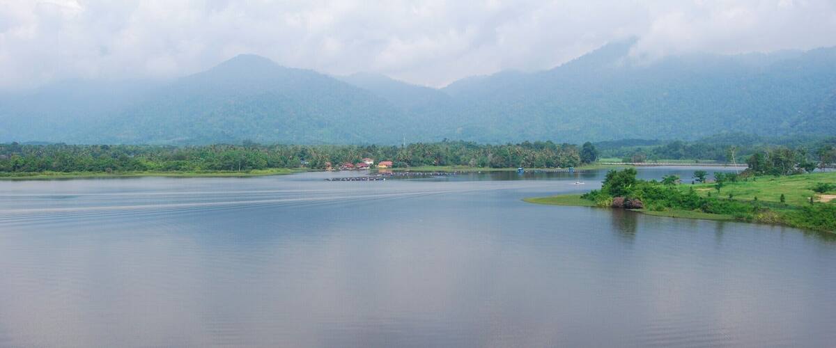 A calm lake with mountains in the background and a small village on the shore.