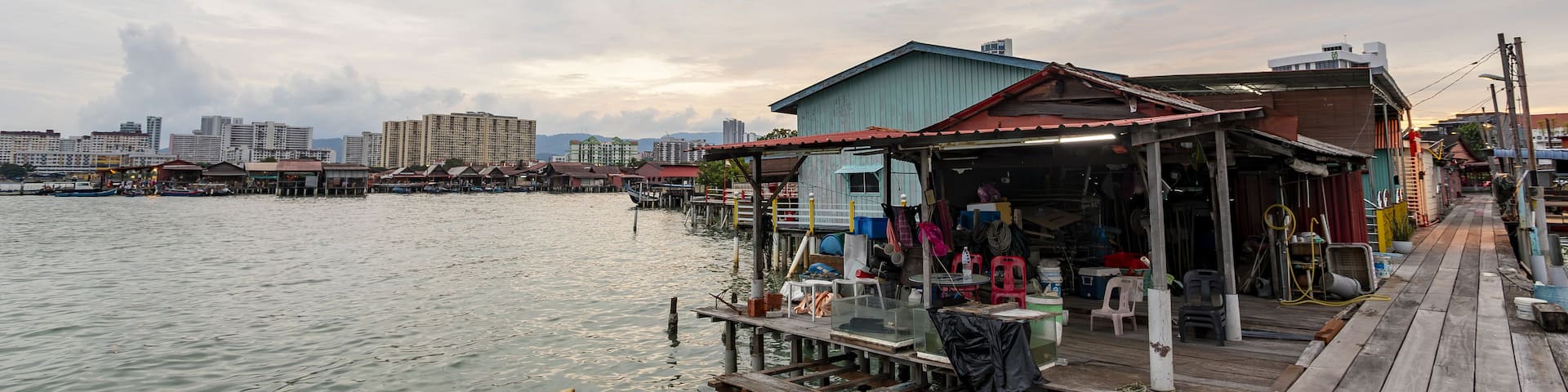 A waterfront with a wooden dock, a small shop, and a cityscape in the background.