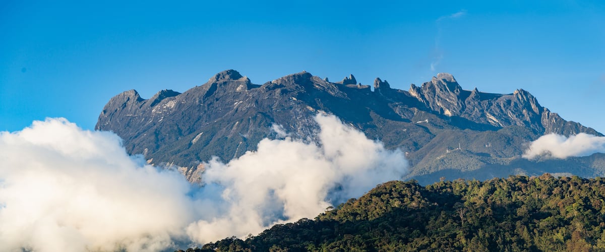 A rugged mountain range with dense forested slopes and clouds at the base.