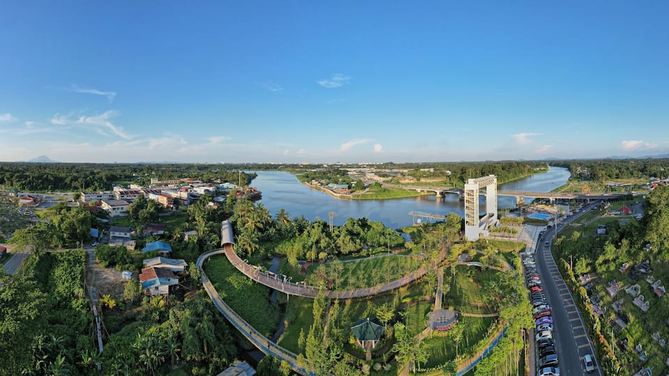 An aerial view of a town with a river, a bridge, and a large building with a red roof.