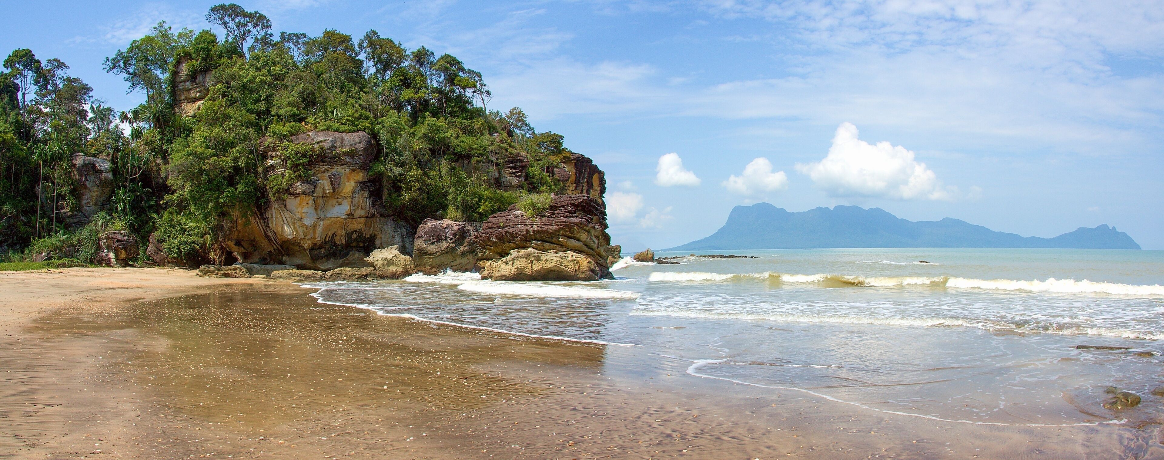 A beach with a rocky cliff and waves.
