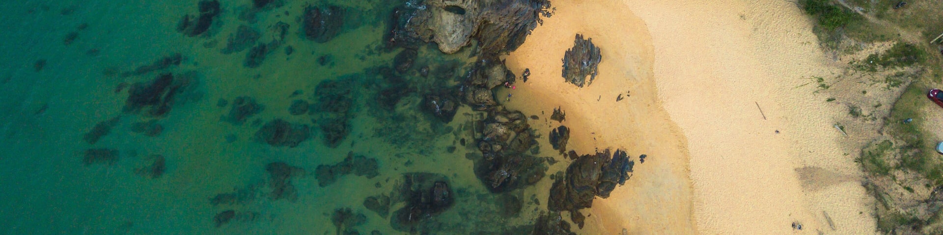 A tropical beach with clear turquoise water, rocky outcrops, and palm trees.