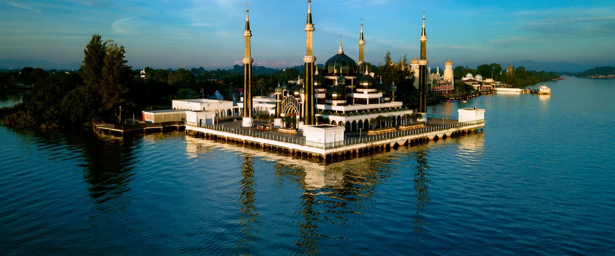 A mosque with multiple minarets on an island in a body of water.