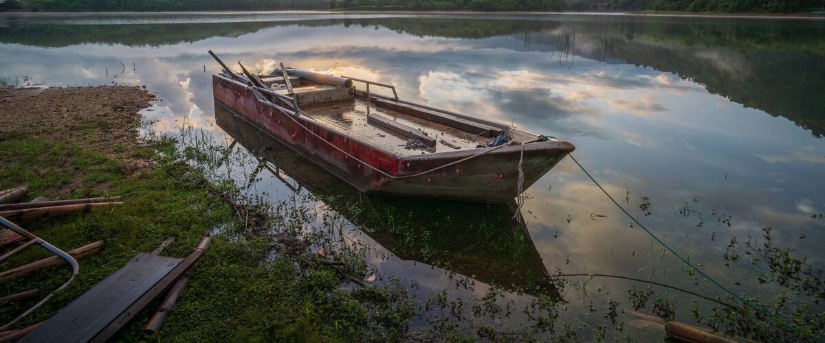 A calm lake with a small boat tied to the shore, surrounded by lush greenery and hills.