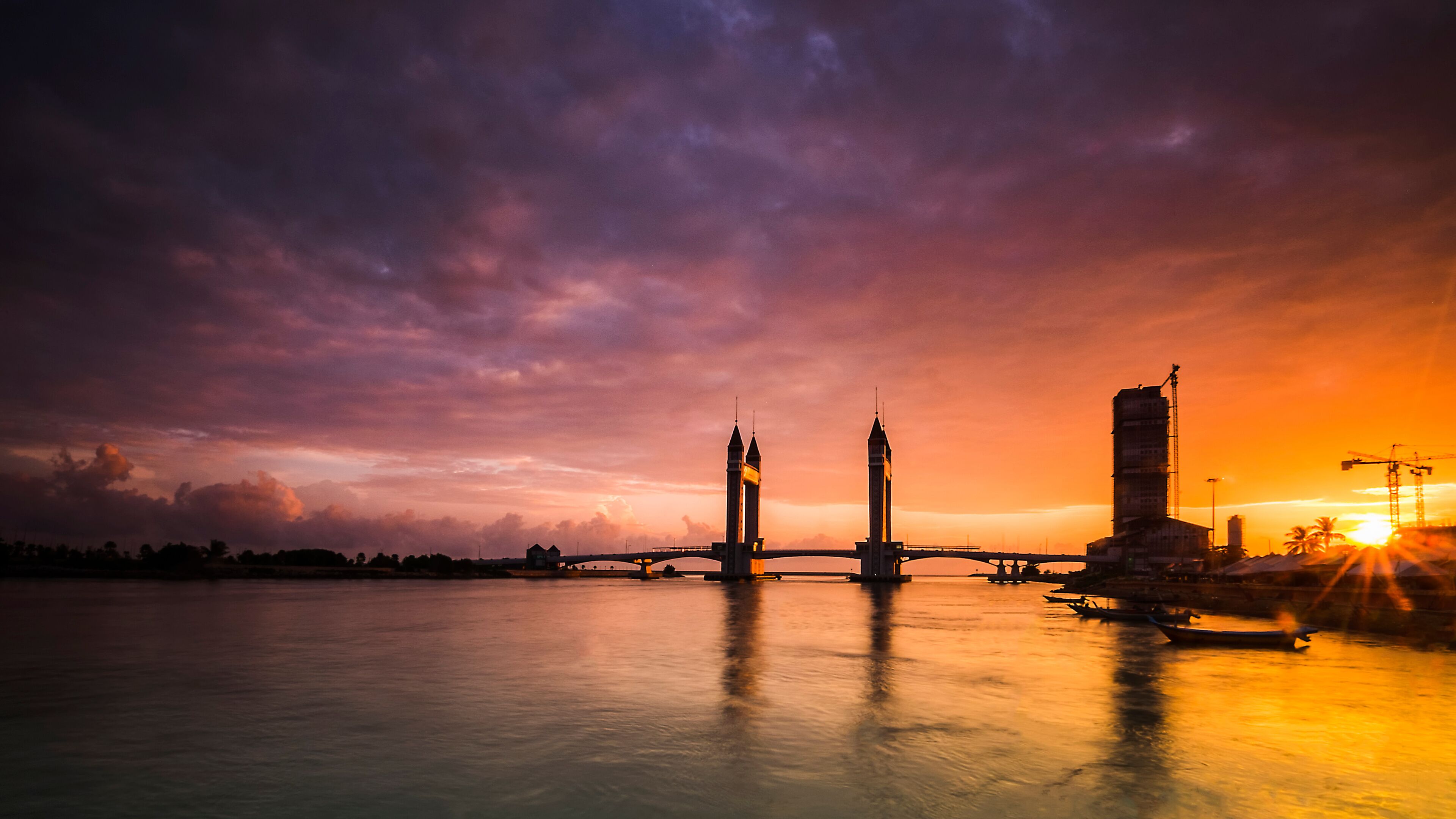 A sunset over a river with a bridge, two towers, and a building.