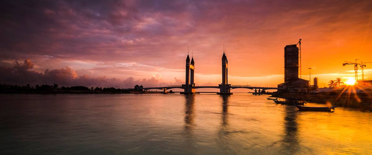 A sunset over a river with a bridge, two towers, and a building.