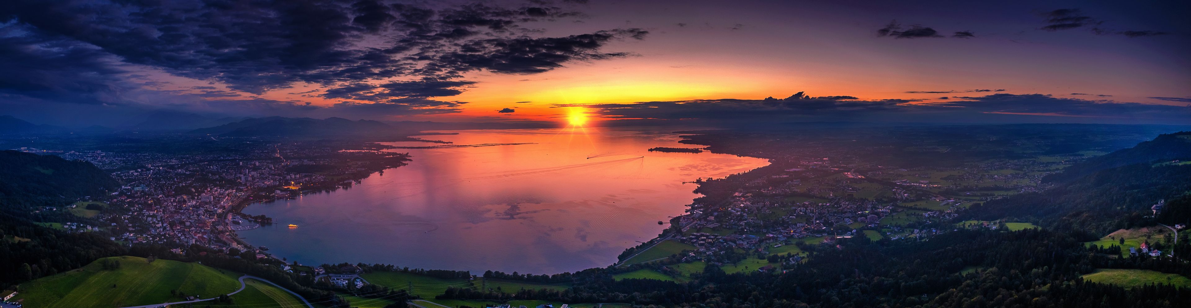 A sunset over a lake with a town in the foreground and mountains in the background.